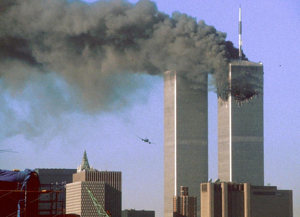 United Airlines Flight 175 flies low toward the South Tower of the World Trade Center, shortly before slamming into the structure. The north tower burns after an earlier attack by a hijacked airliner in New York City, on September 11, 2001